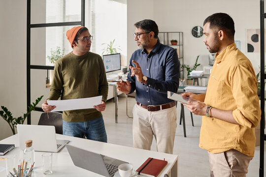 Medium long shot of three Indian men working in modern office discussing business project