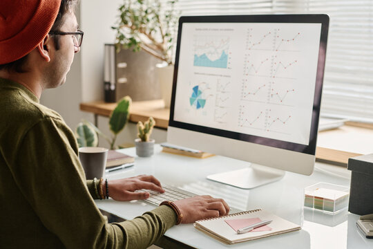 Young man wearing casual clothes working with trading stats on desktop computer in modern office