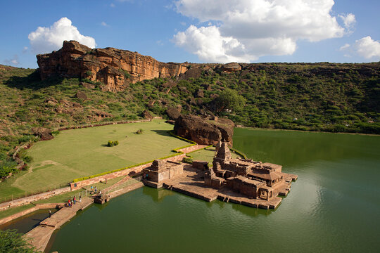 Aerial view of the ancient Bhootnath temples complex reflected on the still, green waters of the lake, shadowed by rugged cliffs, Badami, Karnataka, India.