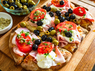 Pinsa Romana with boiled ham, burrata cheese, tomatoes and olives on wooden table