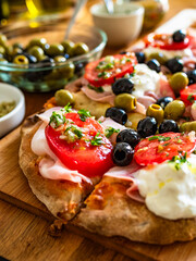 Pinsa Romana with boiled ham, burrata cheese, tomatoes and olives on wooden table