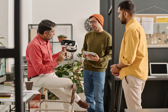 Medium long shot of group of three Indian men coworking on new project in IT company office