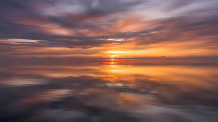 Fototapeta premium Dramatic sunset over calm water reflecting fiery clouds