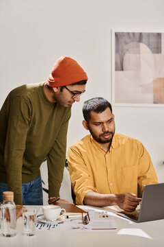 Vertical shot of two young Indian men wearing casual clothes working together on new business strategy