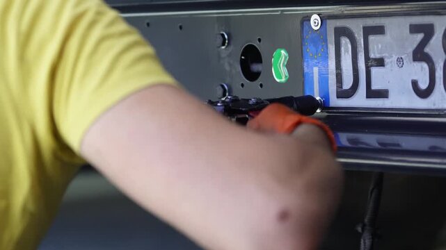 Car dealership employee installs new license plate on car in workshop, car repair and maintenance concept.