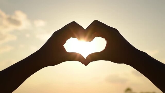 A heartwarming clip of hands forming a heart shape against a golden sunset, symbolizing love and connection, perfect for romantic or sentimental projects