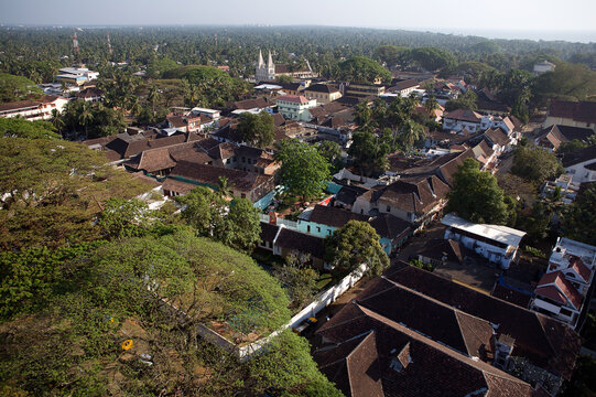 Aerial view of the picturesque townscape reveals terracotta roofs nestled among lush greenery, with twin church spires rising in the distance, Kochi, Kerala, India.