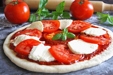 Raw Caprese pizza with tomato, mozzarella and basil leaves. Selective focus
