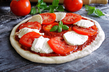 Raw Caprese pizza with tomato, mozzarella and basil leaves. Selective focus
