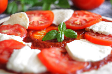 Raw Caprese pizza with tomato, mozzarella and basil leaves. Selective focus

