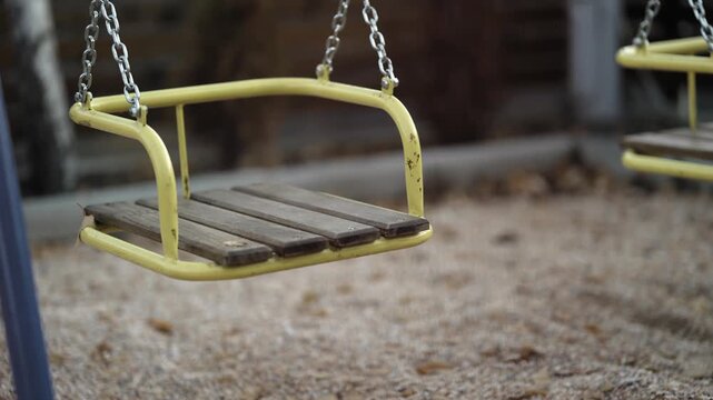 Swinging empty yellow swing with a wooden seat, hanging on chains