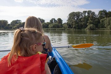 Fototapeta premium Mother and daughter paddling a canoe on calm river in summer nature