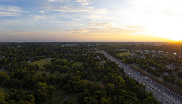 Aerial view of golden light kissing the treetops as cars stream along the highway, painting streaks through the verdant landscape, Charlotte, North Carolina, United States.