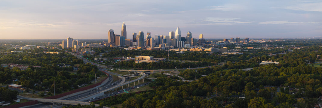 Aerial view of a sprawling cityscape with gleaming skyscrapers piercing the horizon, juxtaposed against the lush green canopy and winding highways, Charlotte, North Carolina, United States.