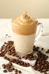 Delicious dalgona coffee in glass cup and beans on table, closeup