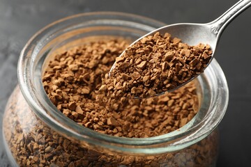 Adding granulated instant coffee from spoon into jar on dark table, closeup