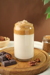 Delicious dalgona coffee in glass, pieces of chocolate and walnuts on table, closeup