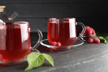 Aromatic raspberry tea in glass cups, berries and green leaves on black table, closeup