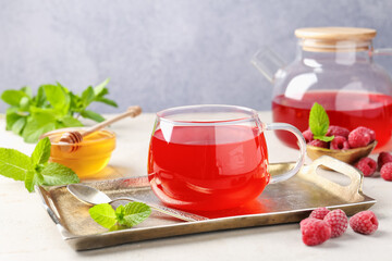 Tasty raspberry tea, berries, honey and mint on light grey table, closeup