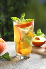 Tasty iced peach tea in glass, fresh fruits and mint on grey table, closeup