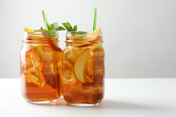 Refreshing iced peach tea with mint in mason jars on white table, closeup. Space for text