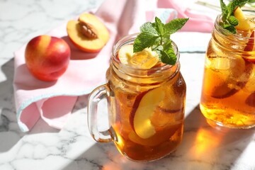 Refreshing iced peach tea with mint in mason jars on white marble table, closeup