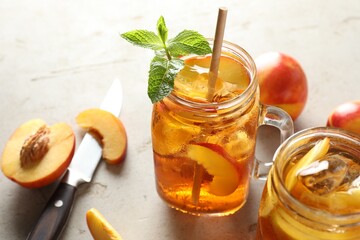 Refreshing iced peach tea with mint in mason jar and fresh fruits on light table, closeup
