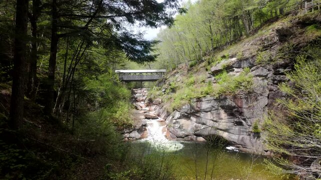 A wide view of Flume Gorge covered bridge spanning rocky stream and forest trail, establishing static