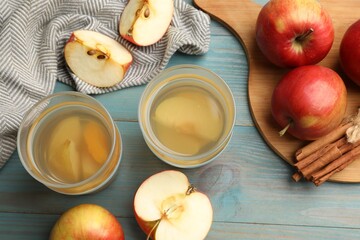 Tasty compot in glasses, fresh apples and cinnamon on light blue wooden table, flat lay