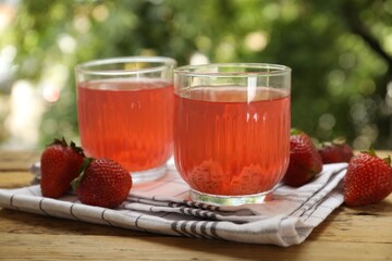 Tasty compot in glasses and fresh strawberries on wooden table outdoors, closeup