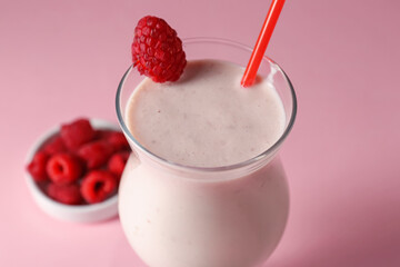 Tasty raspberry milkshake in glass and berries on pink background, closeup