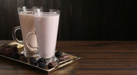 Different tasty milkshakes in glasses and ingredients on wooden table, space for text