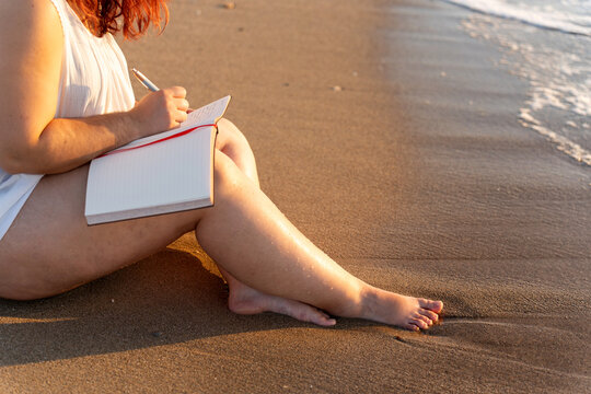 Woman writing in notebook on beach at sunset, embracing body positivity - Powered by Adobe