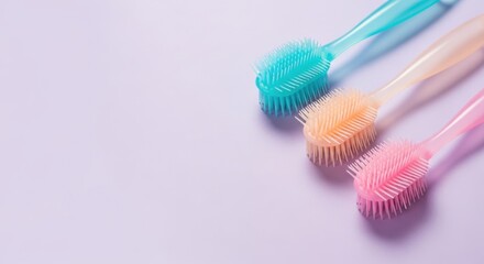 Three colorful silicone brushes in pastel shades of blue, peach, and pink, arranged diagonally on a light purple background