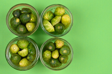 Four open jars filled with fresh green cucumbers on a solid green background, with ample negative space to the right