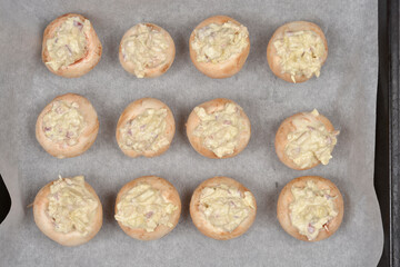 Twelve stuffed button mushrooms are arranged in rows on baking paper, ready for the oven