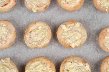 A detailed close-up shows densely arranged stuffed button mushrooms on baking paper, ready for baking