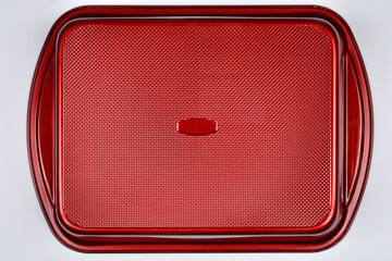 A red baking pan with a textured bottom, ready for use, is shown on a neutral light gray background