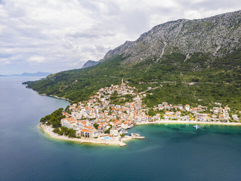 Aerial view of terracotta rooftops cascading down to meet the turquoise Adriatic Sea, embraced by the rugged, verdant slopes of Biokovo Mountain, Igrane, Split-Dalmatia County, Croatia.