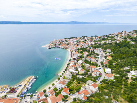 Aerial view of the turquoise sea gently embracing the red-roofed buildings of Igrane, nestled along the Croatian coastline under a vast sky, Igrane, Split-Dalmatia County, Croatia.