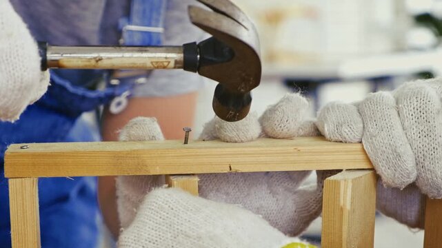 Close-up of hands in protective gloves hammering a nail into wood, capturing teamwork, skill, and craftsmanship in carpentry. Symbolizes precision, construction, and family work ethic.