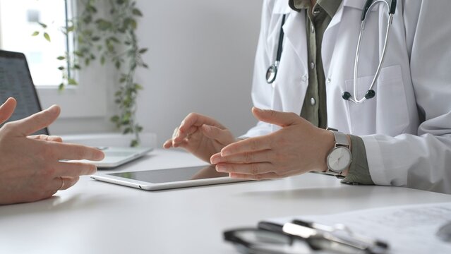 Doctor using digital tablet to show test results to a patient during a medical consultation in hospital office, healthcare and technology concept. Medicine and health care concept