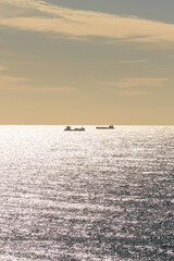 Obraz premium Cargo ships on a shimmering sea under a sunset sky