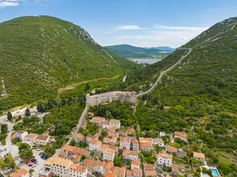 Aerial view of ancient fortress walls snaking across verdant hillsides, embracing the quaint town below in a tapestry of terracotta roofs, Mali Ston, Dubrovnik-Neretva County, Croatia.