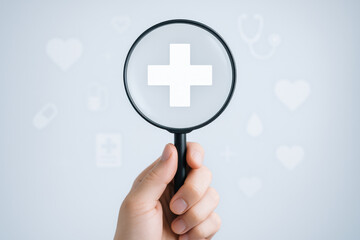 Obraz premium Hand holds magnifying glass focusing on medical cross symbol representing life and insurance