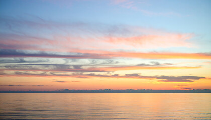 Naklejka premium Serene Sunset Sky with Layered Pink and Orange Clouds over Calm Water.