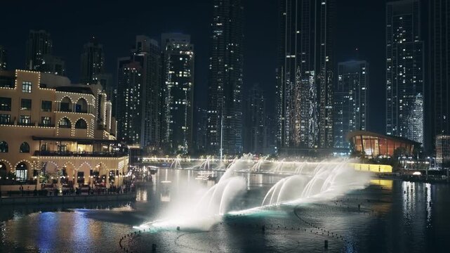 Aerial night view of water fountain show in Dubai Downtown near the Opera with illuminated skyscrapers at background