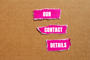 Our contact details message written on ripped torn pink paper pieces on cardboard background. Conceptual our contact details symbol. Copy space.