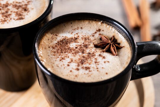 Chai Latte in Black Mug with Spices( star anise and cinnamon) on wooden table. Close up
