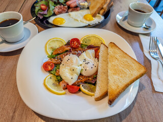 Healthy and delicious brunch plate with poached eggs, smoked salmon, fresh salad, and toast, served with coffee.Breakfast date at restaurant: one plate with poached eggs and another with fried eggs